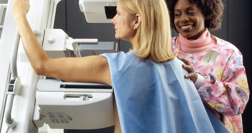 smiling woman standing near another woman beside mammogram machine