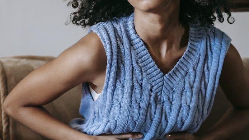 Young African American female sitting on couch at home while having acute pain in stomach